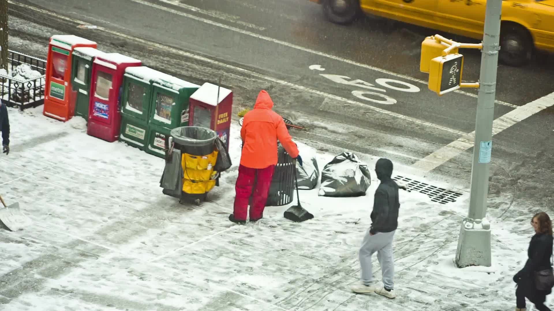 sanitation man in orange jacket shoveling snow on corner in blizzard on winter day snowing in Manhattan NYC