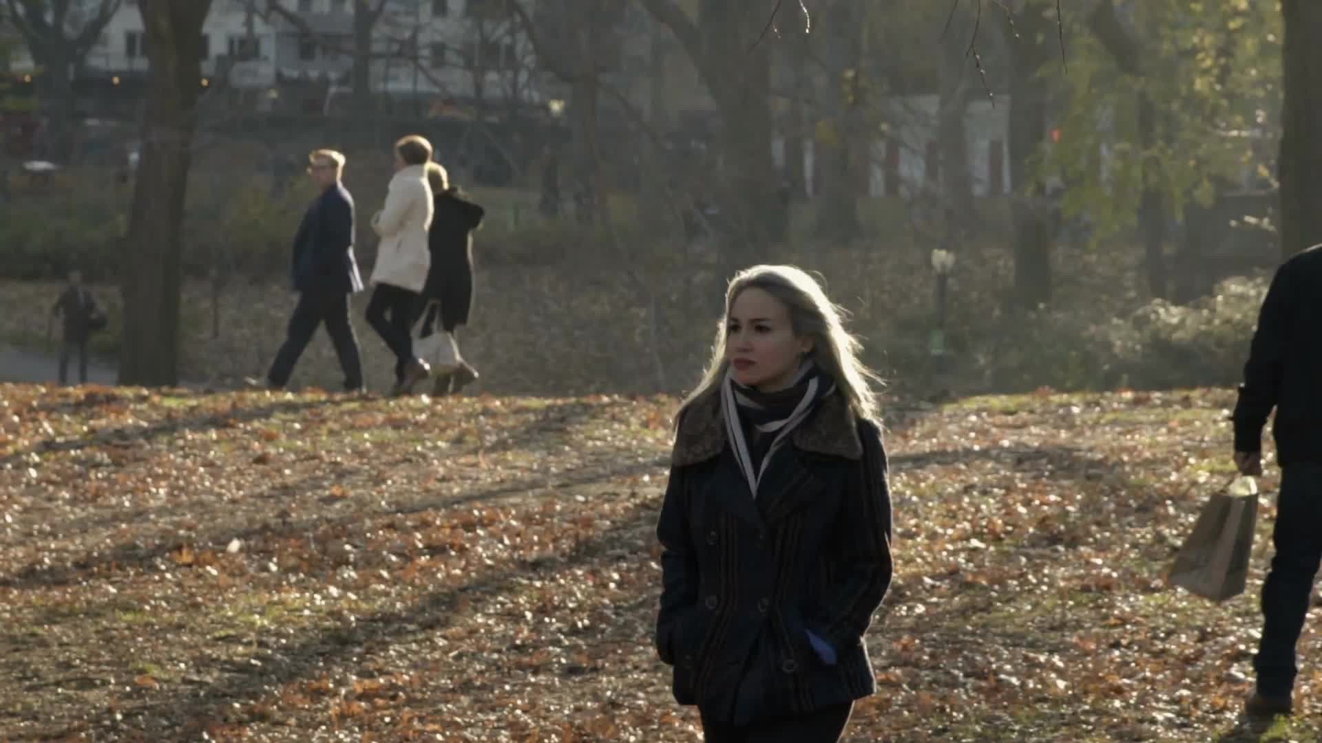 attractive woman in autumn walking through Central Park on cold fall winter day with trees and leaves on ground, slow motion