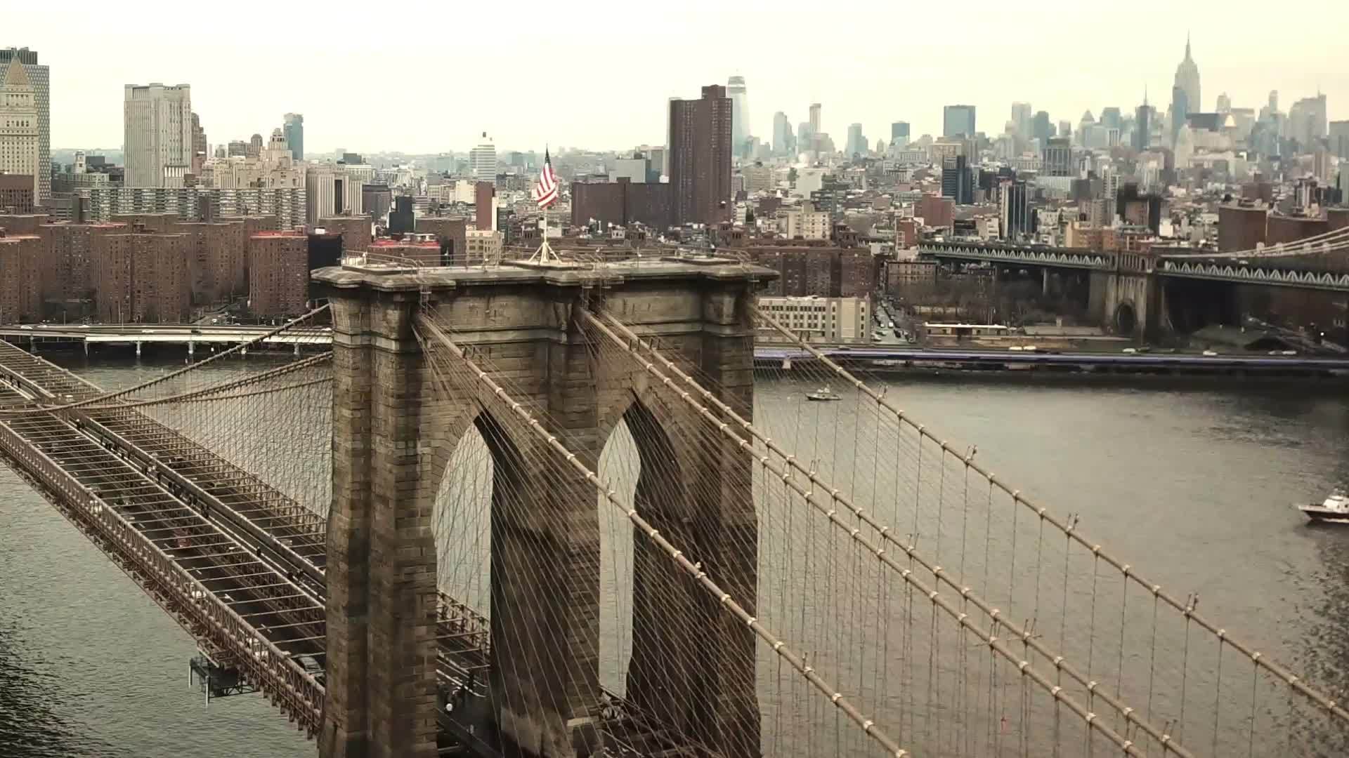 aerial flying over American flag on Brooklyn Bridge straight ahead toward Manhattan buildings on East River in 1080 HD