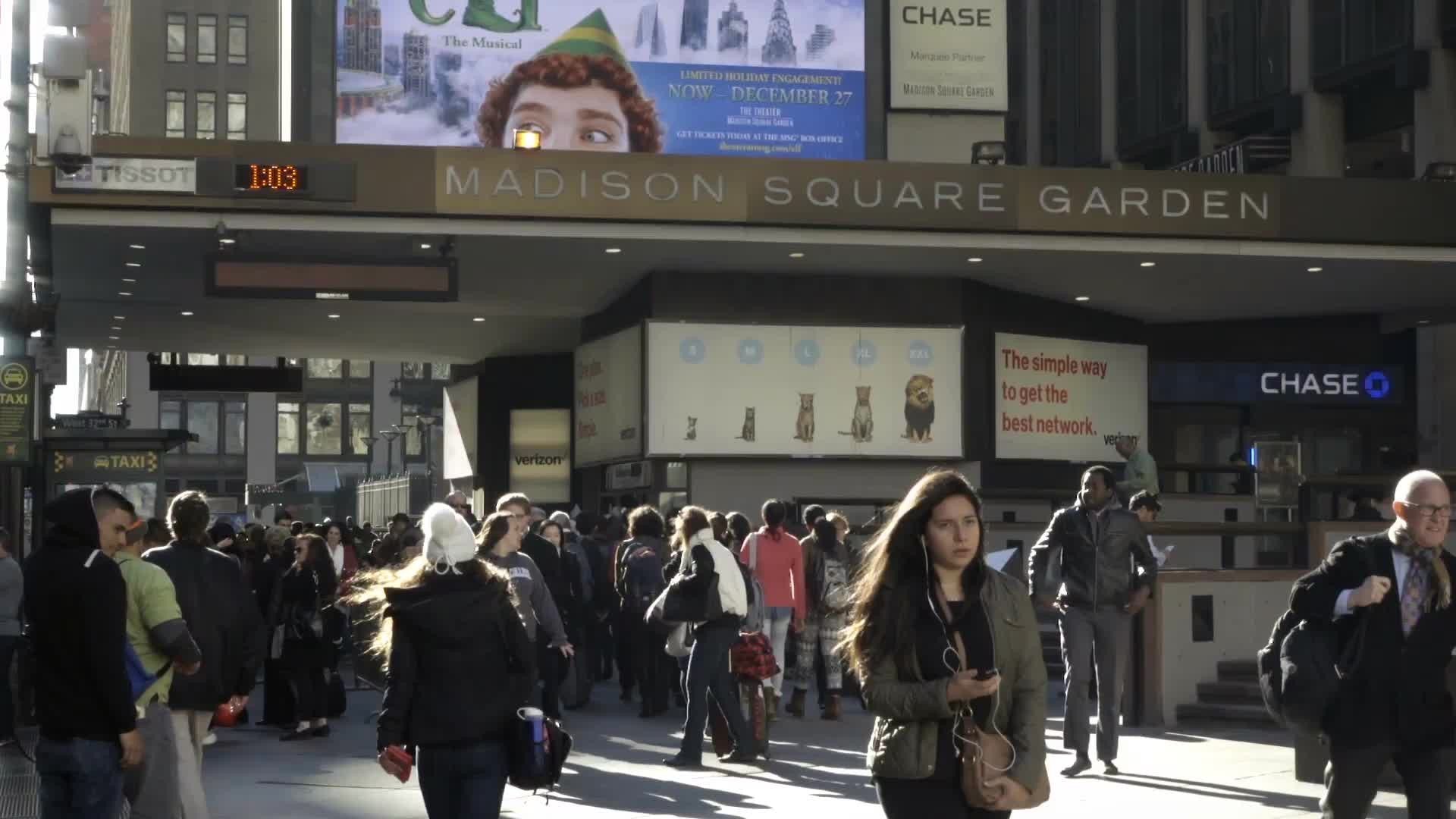 Madison Square Garden on bright sunny fall day - people walking outside in slow motion - woman on headphones in NYC