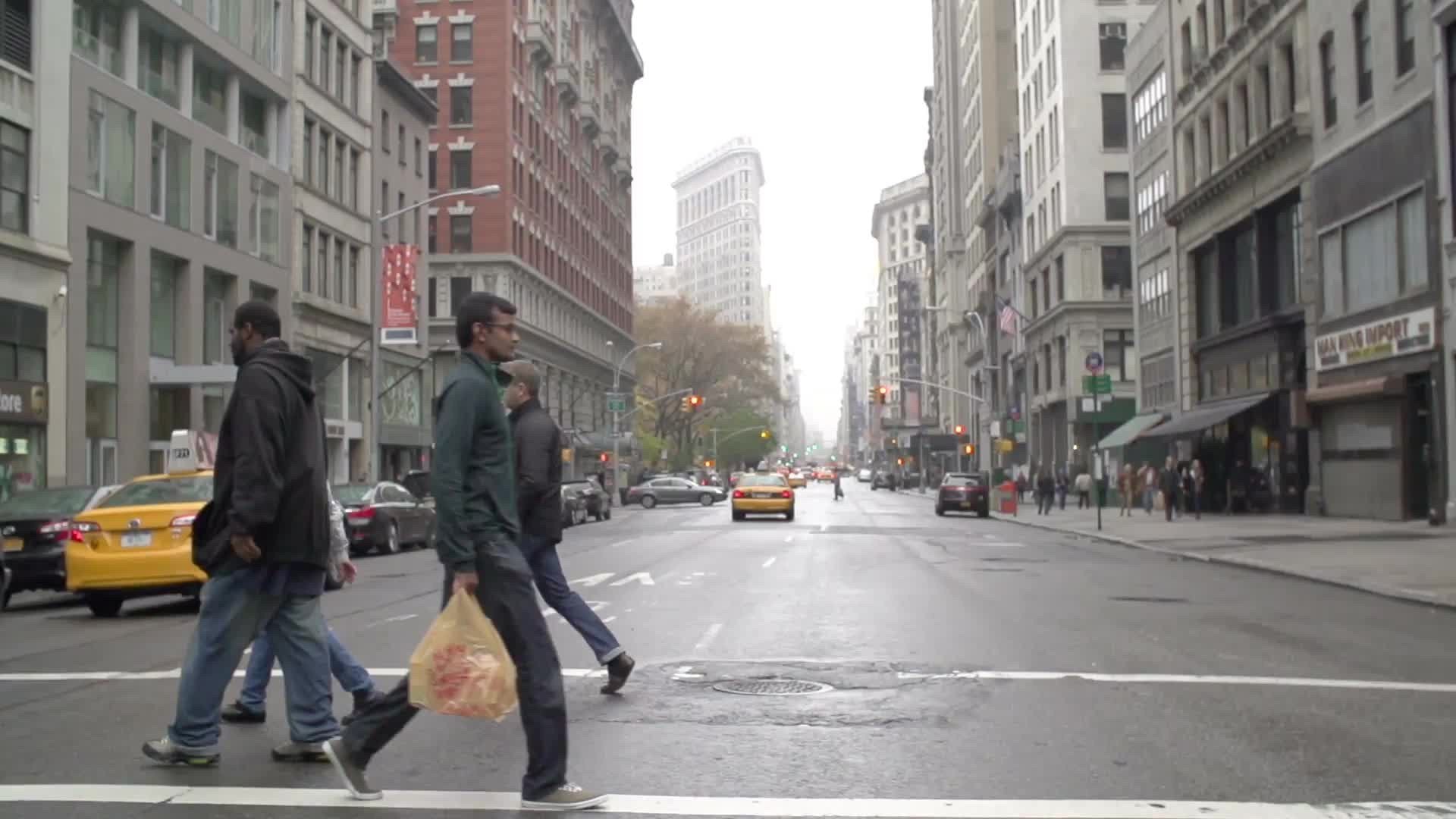 people crossing 5th Ave with Flatiron Building in background on muggy fall day in Manhattan NYC