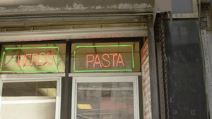 neon heros and pasta sign in pizzeria deli shop with cook in uniform in window