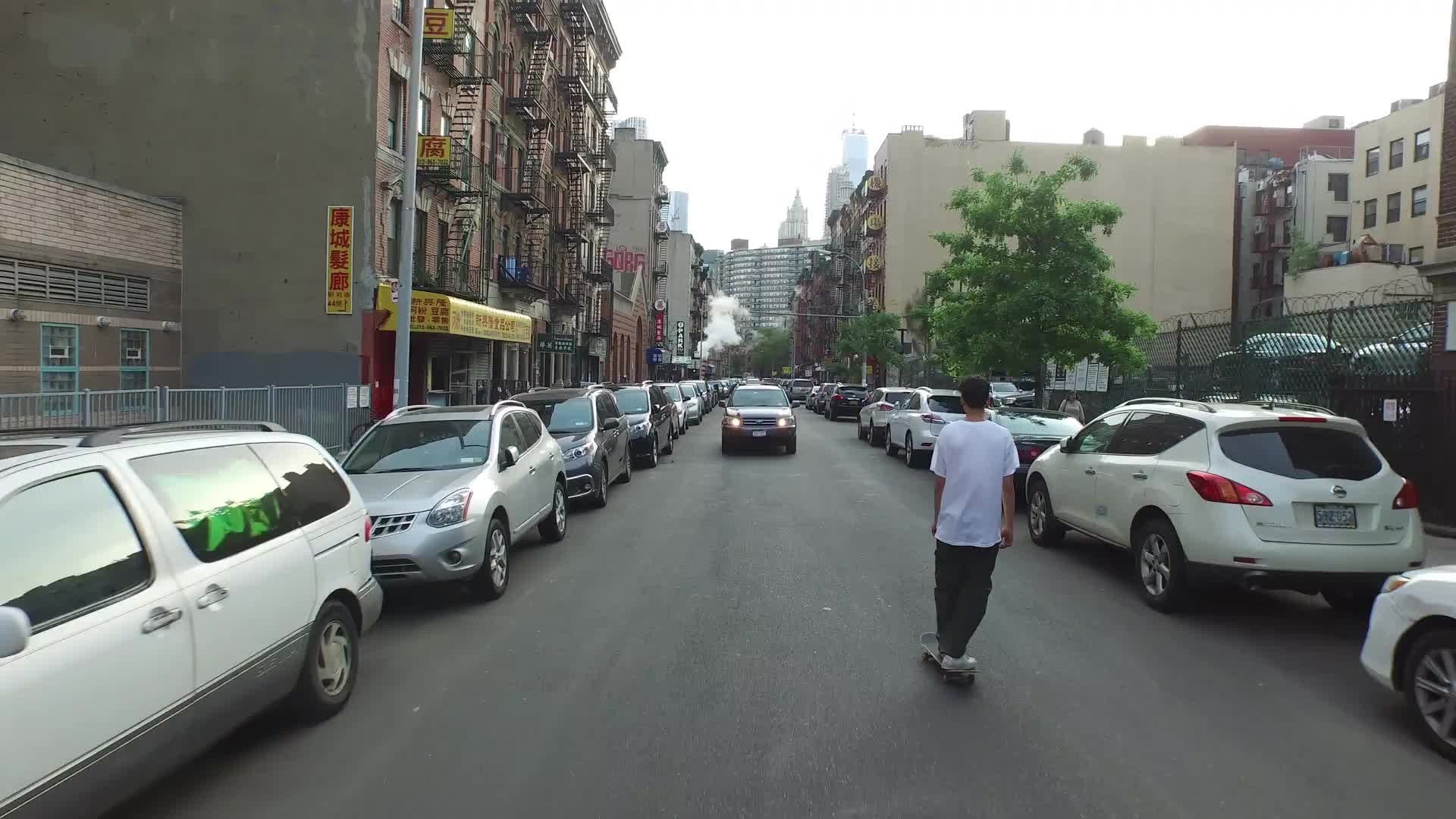 aerial of kid skating down Chinatown street rising to view of Manhattan skyscrapers