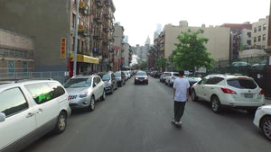 aerial of kid skating down Chinatown street rising to view of Manhattan skyscrapers