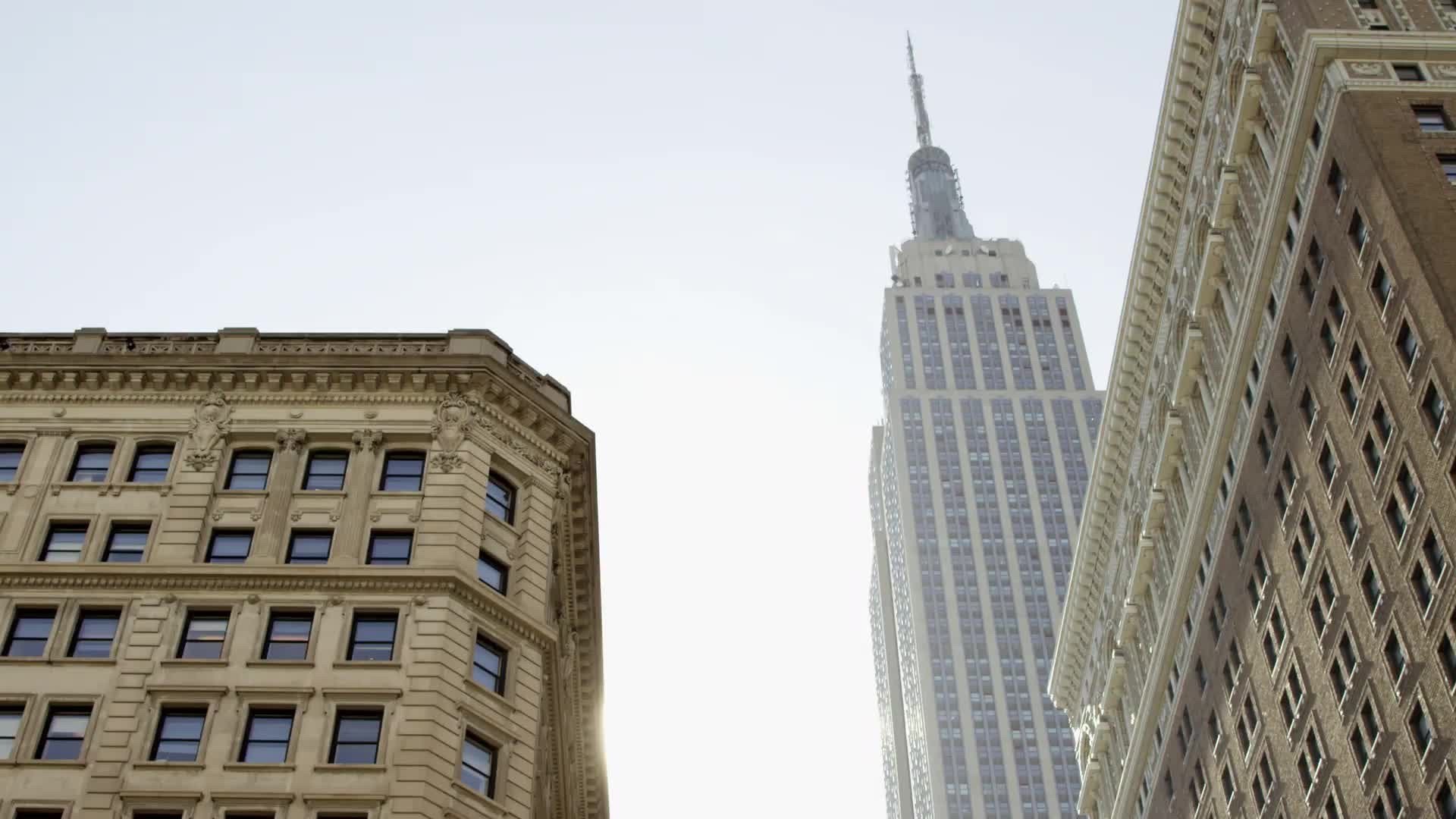 Empire State Building tilting down to NYPD police officers by car on street in Herald Square