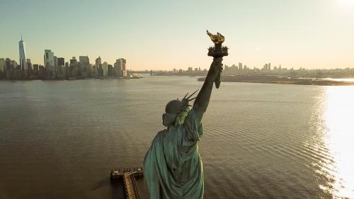 Statue of Liberty at golden sunset with Manhattan skyline in background - aerial on New York Harbor in NYC