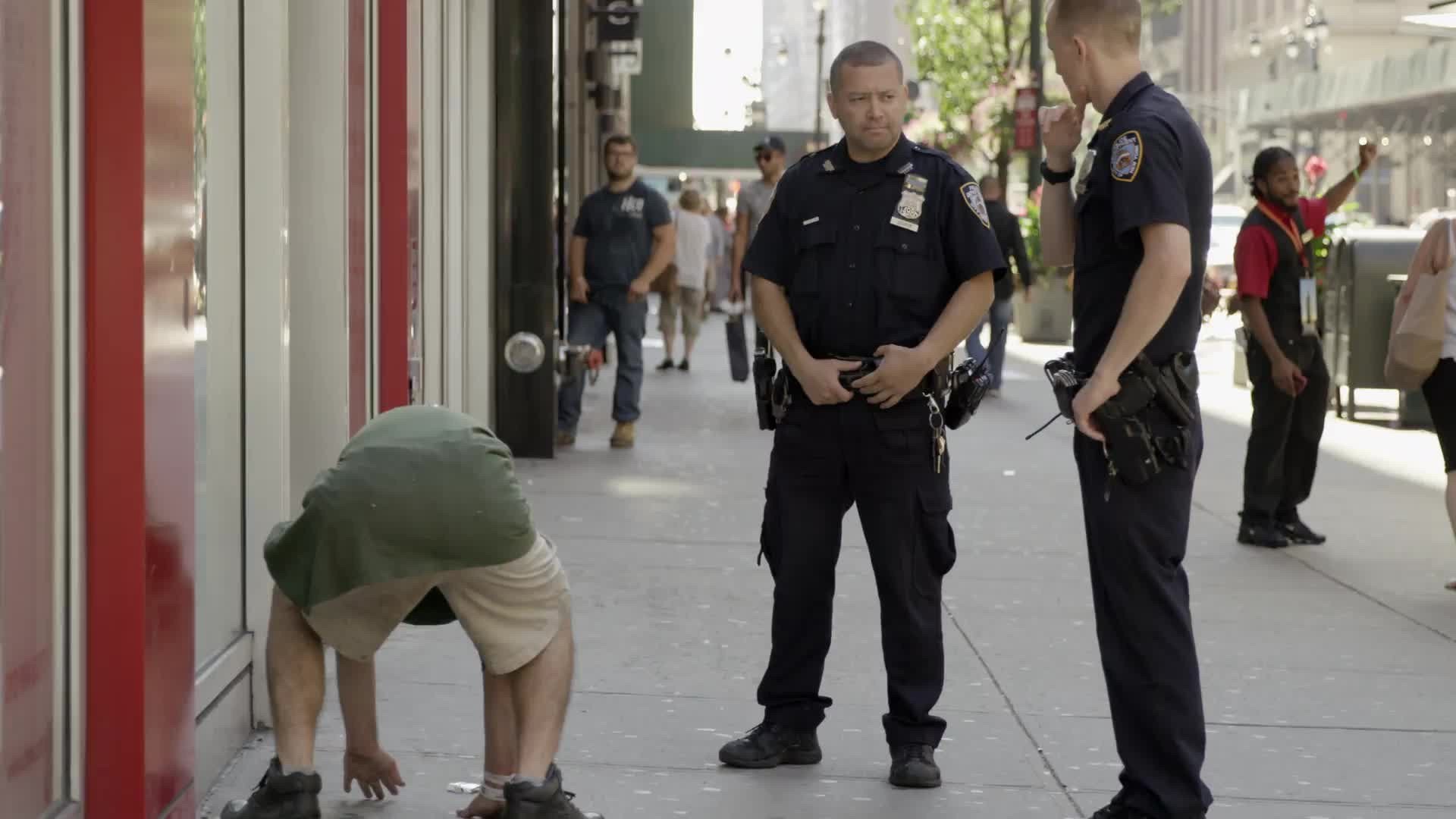 NYPD police officers and drunk homeless man getting up off street in Midtown Manhattan on summer day