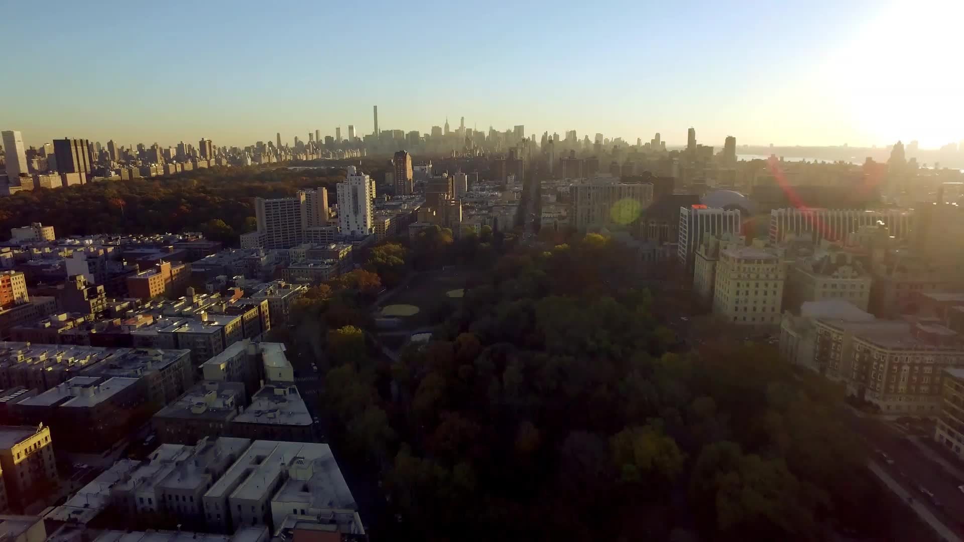 aerial over trees uptown with Manhattan skyline in distance at sunset in NYC