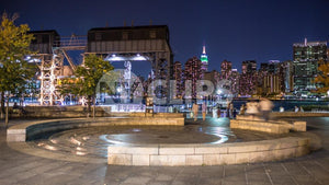 Manhattan skyline at night view from Long Island City circle stone benches and fountain in LIC