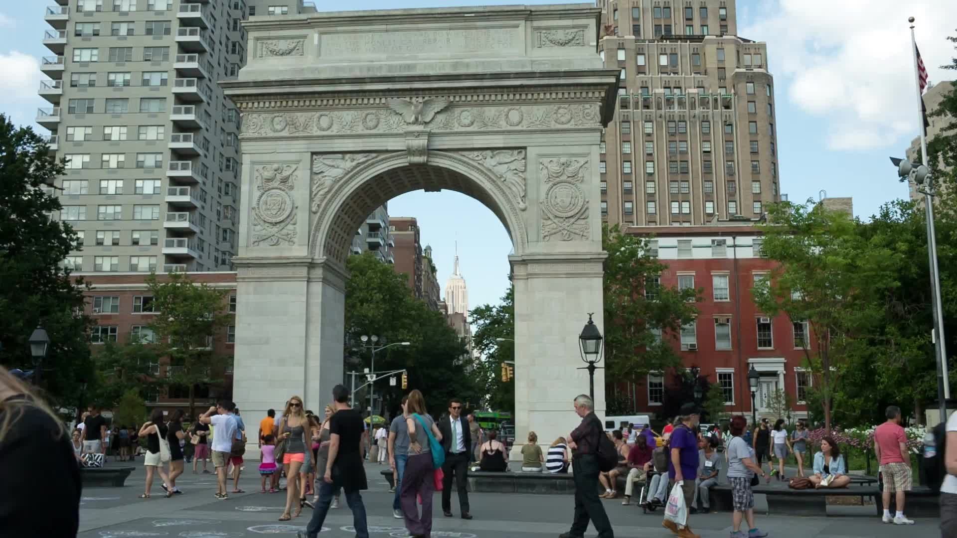 people walking past Washington Square Park arch on summer day in late afternoon in New York City