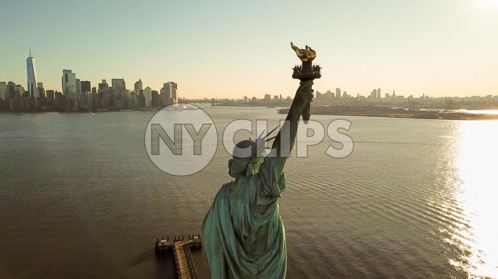 Statue of Liberty at golden sunset with Manhattan skyline in background - aerial on New York Harbor in NYC