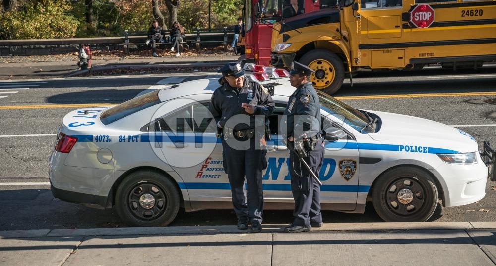 NYPD officers chatting leaning on police car on sunny Fall day in NYC