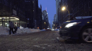 Lower 5th Ave in winter at night - low view of slush on street - snow on ground with cars and taxi cab driving by in NYC