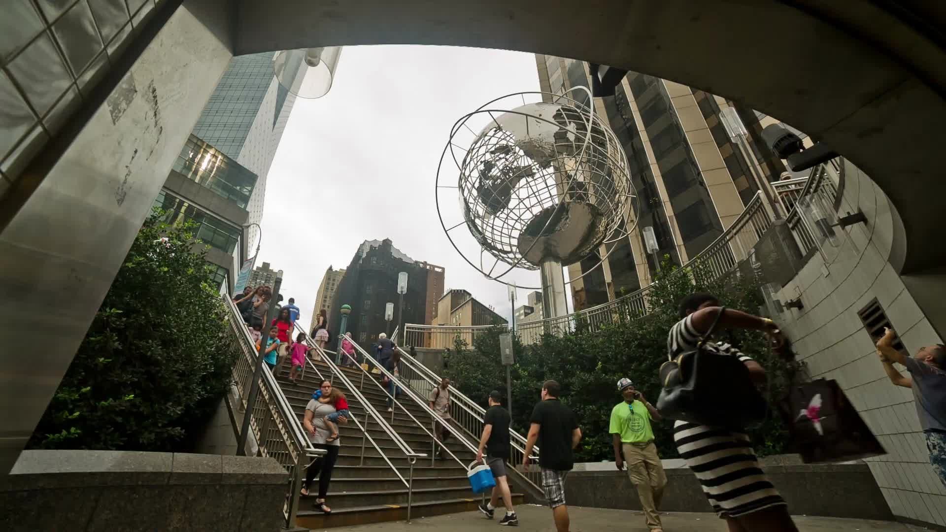 Columbus Circle subway station with Steel Globe sculpture and people walking down stairs on summer day in NYC