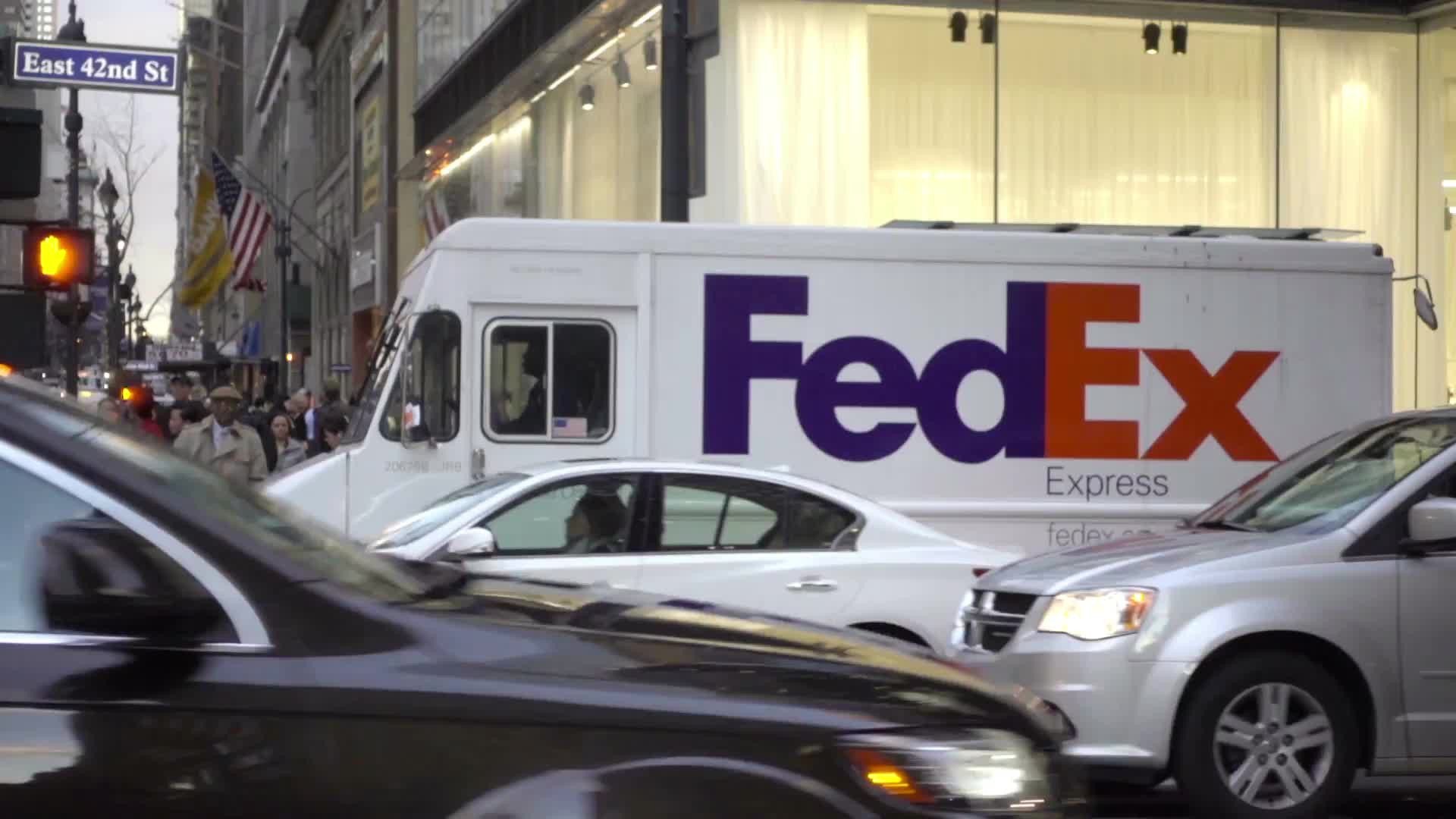 Fed Ex truck driving in Midtown Manhattan with cars and taxi cabs and NYPD traffic cop, busy intersection in NYC