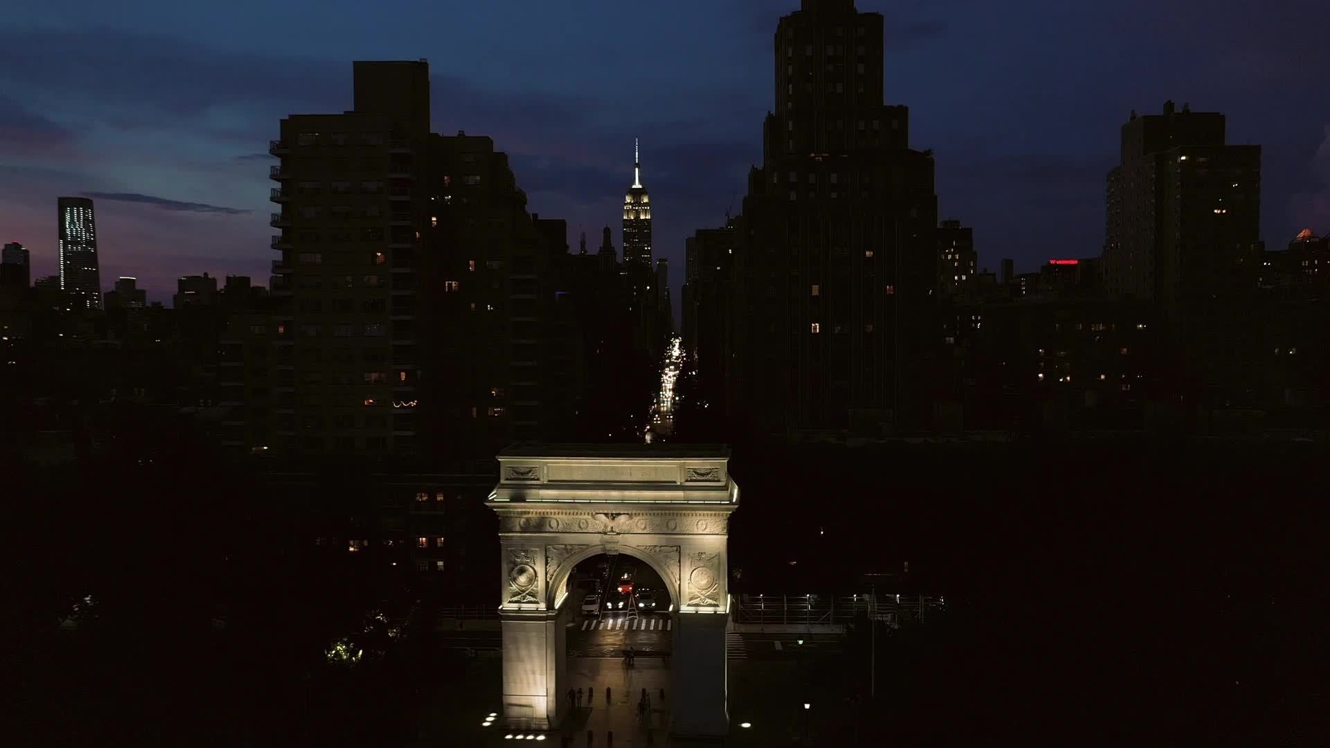 aerial moving toward Empire State building over arch in Washington Square Park at night NYC
