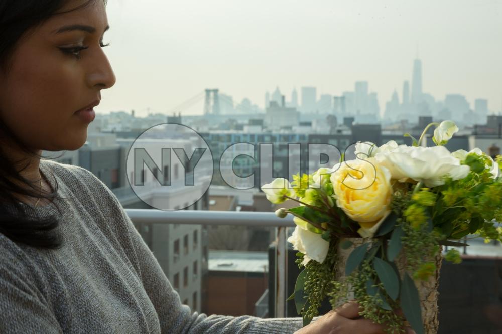 Brooklyn woman arranging flowers on rooftop with Manhattan skyline in background in New York City