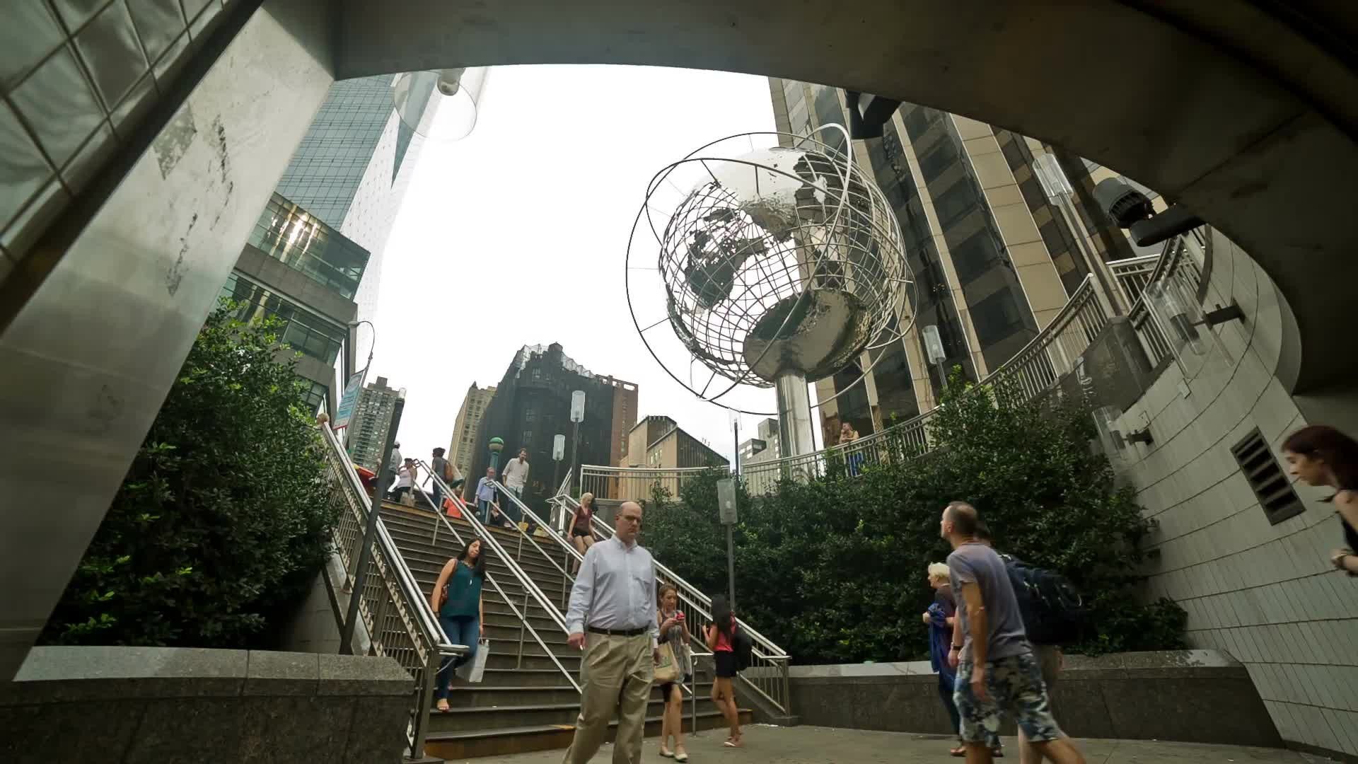 people entering and exiting Columbus Circle subway station stairs with Steel Globe Sculpture overhead on summer day in NYC