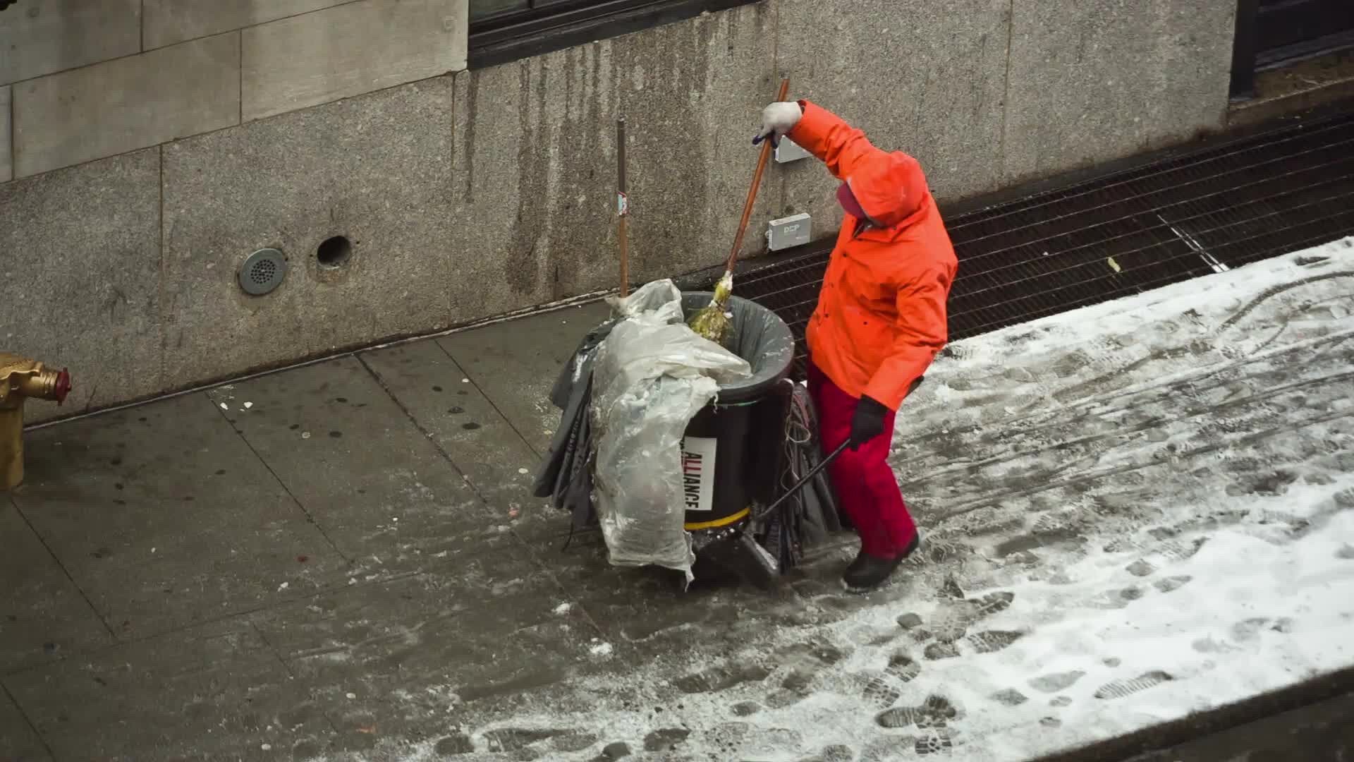 street cleaner man in orange coat on cold winter day with snow on ground in NYC