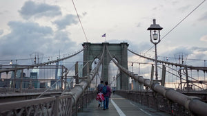 people walking across Brooklyn Bridge with American flag on tower at sunset in summer NYC
