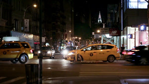 taxi cabs driving on Houston Street busy intersection with Chrysler Building in background at night downtown