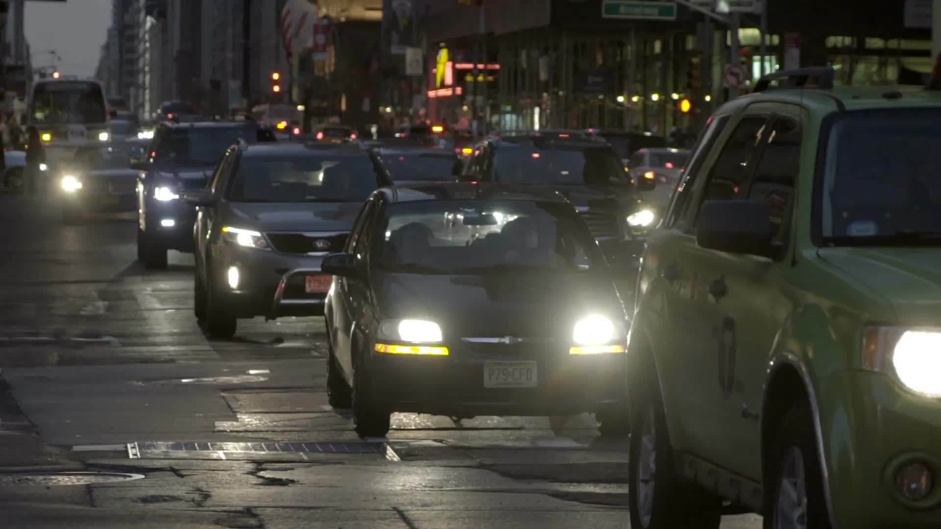 Midtown Manhattan street with bright headlights on cars in traffic in early evening, slow motion Manhattan NYC