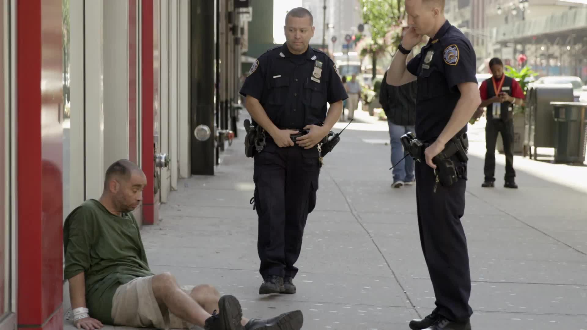 police standing over drunk man sitting on sidewalk in Midtown Manhattan on summer day in NYC