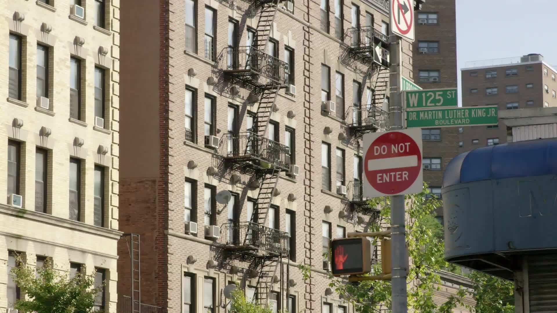 125th Street sign Martin Luther King Jr. Blvd do not enter signs tenements buildings with fire escapes in Harlem with cars driving by in 4K