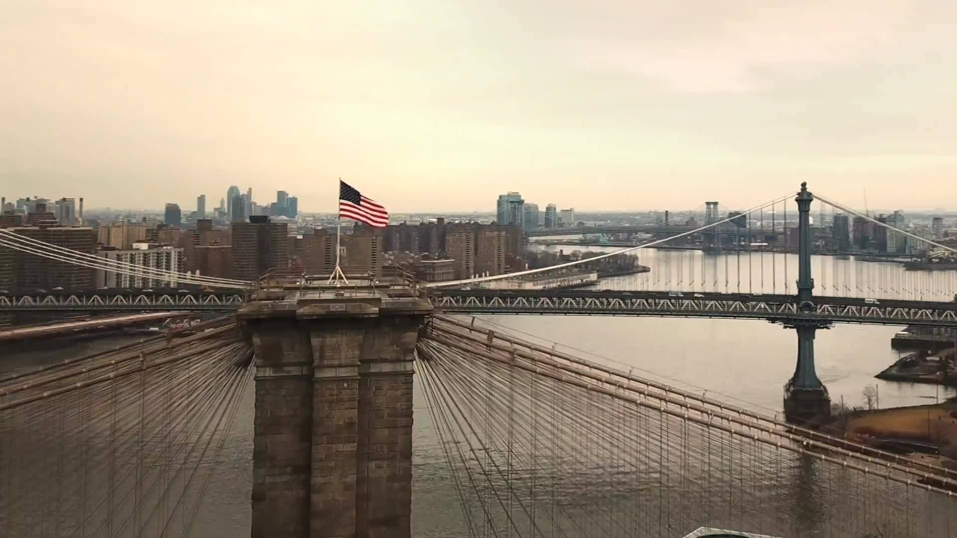 Brooklyn Bridge with American flag aerial circling toward Manhattan skyline with Freedom Tower in 1080 HD