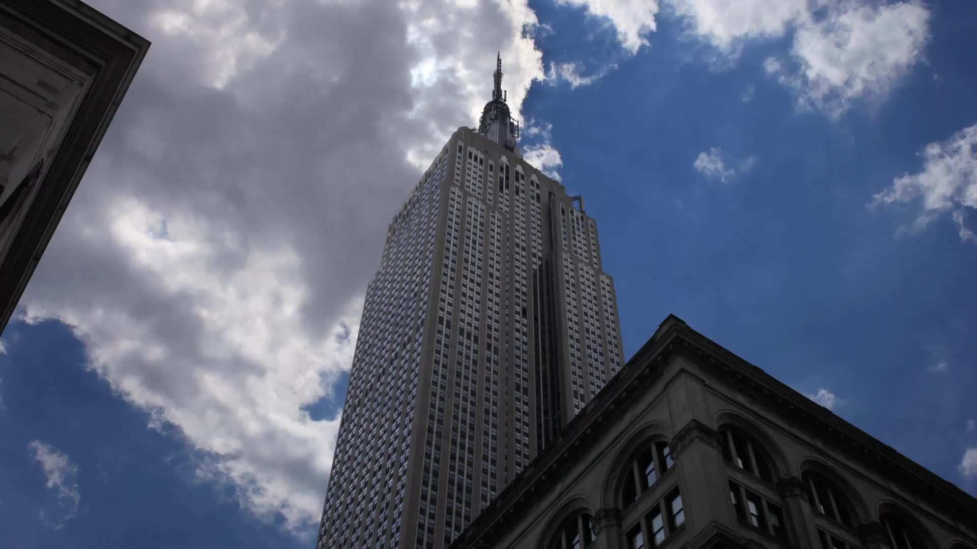 Empire State Building time-lapse upward angle with clouds on blue sky with bright sun and airplane shooting star in Manhattan New York City NYC in 4K and 1080 HD
