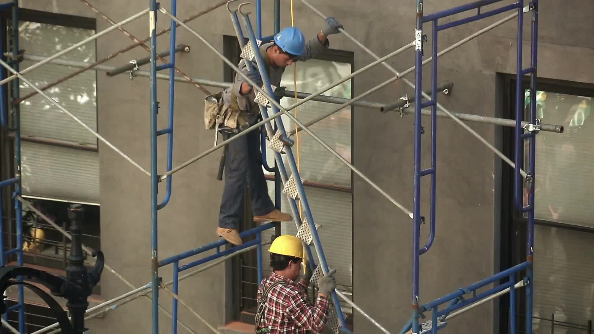 construction workers in hard hats carrying ladder climbing scaffolding on building