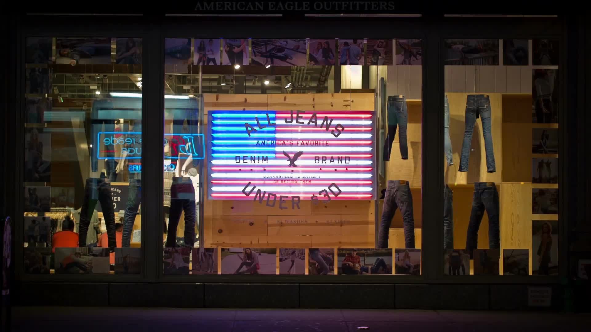 clothing store with rotating jeans display and  American flag LED sign at night on Broadway in NYC