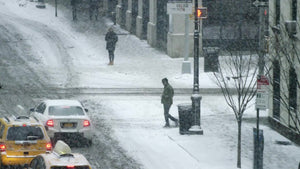 man crossing street in winter blizzard snow storm, snowing on street in far shot slow motion 4K